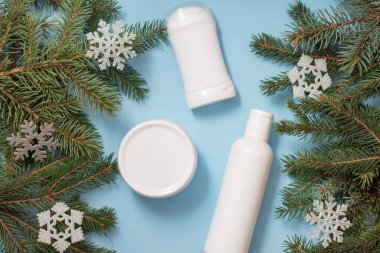 Mavi arka planda kozmetik şişeleri ve kavanozlar Noel ağacı dalları ve oyuncak kar taneleri çerçeveli..