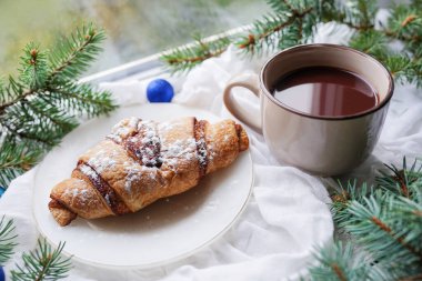 Karlı kış gününde camında ayçöreği olan dumanı tüten bir fincan sıcak kahve. Noel sabahı kavramı