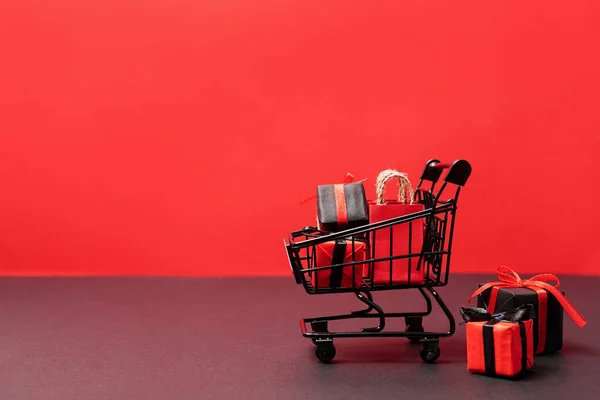 black paper bags and gift boxes in shopping cart on red background, copy space. black friday concept