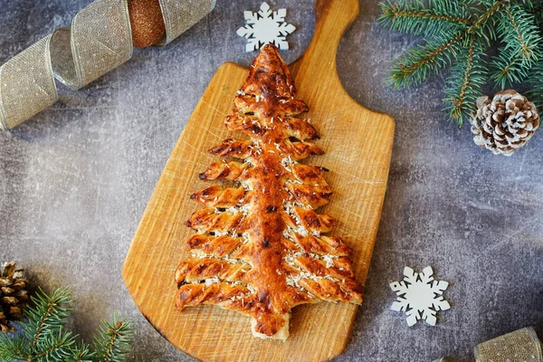 Gri arka planda, köknar dalları ve süslemeleri olan Noel ağacı şeklinde bir turta.