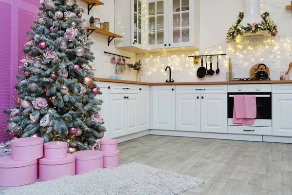 Christmas home decor. Bright interior of white kitchen with pink decorated Christmas tree and garlands.
