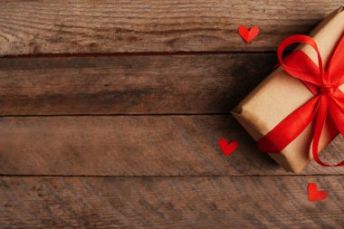 Kağıt tatil hediyesi ve ahşap arka planda kırmızı kalpler Sevgililer Günü tebrik kartı.