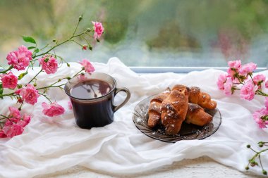 coffee cup and dessert with pink roses on the window sill , romantic morning
