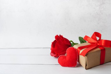 red Gift or present box with bow ribbon, flower rose and heart on white wooden background, greeting card for Valentines day.