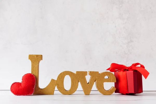 word Love, red Gift or present box with bow ribbon and heart on light stone background, greeting card for Valentines day.