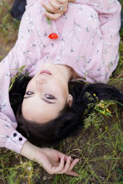 Romantik bir kız çimenlerin üzerinde yatar ve elinde kırmızı bir gelincik tutar.
