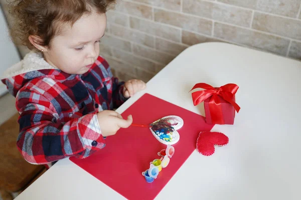 小女孩用油漆装饰手工制作的瓦伦丁心脏 孩子们的Diy 业余爱好的概念 礼物用你自己的手 情人节装饰品 — 图库照片
