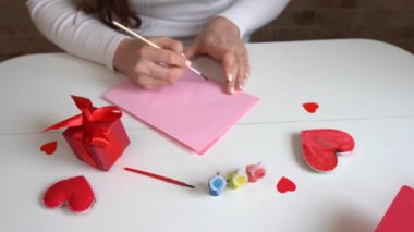Kadın, kırmızı kalp şekilli pembe kağıda aşk mektubu yazıyor. Sevgililer Günü kutlamaları için el yapımı kartpostal. Sevgilileriniz ve arkadaşlarınız için 14 Şubat 'ta mektuplar.