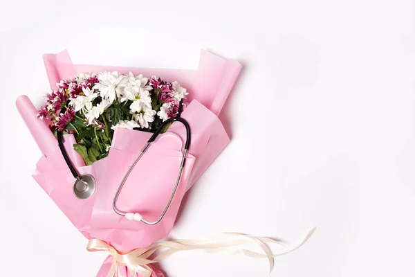 Beyaz arka planda bir buket çiçek ve steteskop. Ulusal Doktor Günü. Hemşire günün kutlu olsun. Kopyalama alanı olan üst görünüm