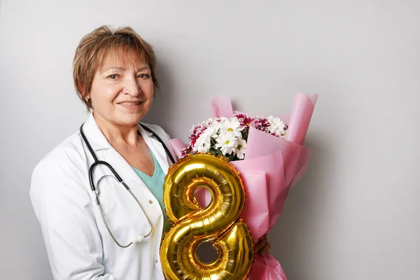 Smiling woman doctor with bouquet of flowers and golden ballon 8 eight , 8 march international women\'s day