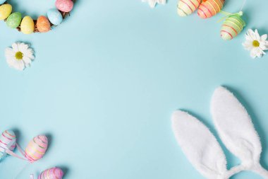 Tavşan kulaklı paskalya çerçevesi, yumurtalar, pastel mavi arka planda beyaz çiçekler. Üst Manzara. Mutlu Paskalyalar. Tebrik kartı.