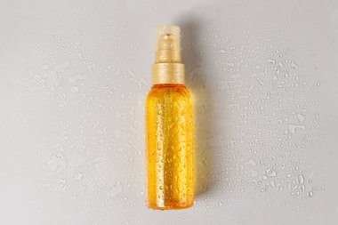 Gri zemin üzerinde su damlaları olan bir şişe şeffaf kozmetik sıvısı.