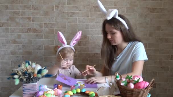 かわいい女の子を持つ魅力的な若い女性がイースターのお祝いの準備をしています ママと娘はウサギの耳を着て家で楽しんでいます — ストック動画