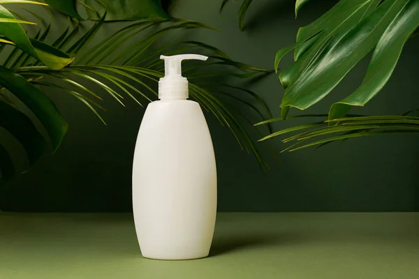 Cosmetic bottle for mockup packaging of skincare product cream, shampoo, conditioner on green background with palm and monstera leaves. Natural beauty product concept