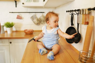 Sevimli çocuk. 1 yaşında. Mutfak odasında büyük bir kaşıkla masada oturuyor.