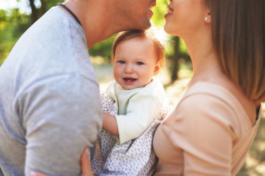 Mutlu genç aile birlikte vakit geçiriyor, anne ve baba dışarıda bebeğiyle yeşil doğada..