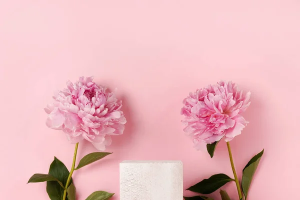 Cosmetics product advertising stand. Exhibition white podium with flowers peonies on a pink background, Empty pedestal to display product packaging. Mockup