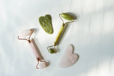 Yüz silindiri ve gua sha masaj aleti. Beyaz masada, gölgeli doğal taşlardan yapılmış.