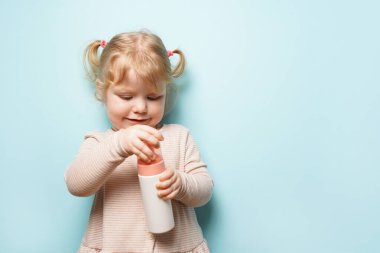 Mavi arka planda duş jeli olan elinde şişe tutan kız çocuğu, çocuklar için vücut bakım ürünleri.