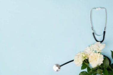 Steteskop ve mavi arka planda bir demet beyaz gül çiçeği. Ulusal Doktor Günü. Hemşire günün kutlu olsun. Kopyalama alanı olan üst görünüm