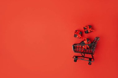 Alışveriş arabasında kırmızı fiyonk olan siyah hediye kutuları, kara Cuma indirimi. kırmızı arkaplan, boşluğu kopyala