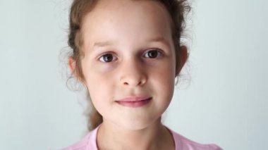 a child girl with a calm expression wearing a pink shirt against a light background