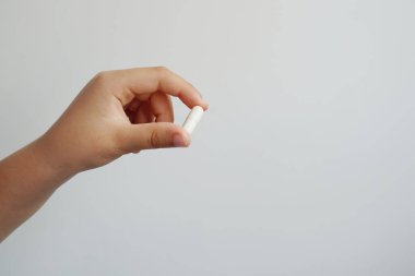 Beyaz kapsülü arka planda tutan bir elin yakın çekimi.