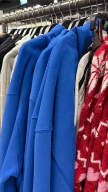 Gri, siyah ve kırmızı desenli giysilerin yanında parlak kapüşonlular asılı duruyor.