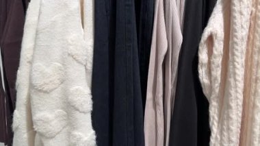 Bir sıra nötr renkli süveter askıda asılı, yumuşak örgü ve dokulu kalp desenleri var.