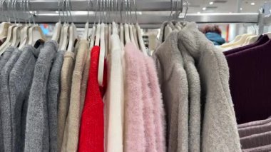 Gri, bej, kırmızı, pembe ve krem rengi kazak karışımı beyaz askılara takılır.