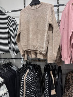 Bej örülmüş süveterler ve çizgili giysiler düzgün düzenlenmiş giyim mağazası bölümünde.