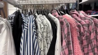 Pembe ekose gömlekli bir elbise askısı, yumuşak örgü, noktalı bluzlar ve mavi çizgili bluzlar.