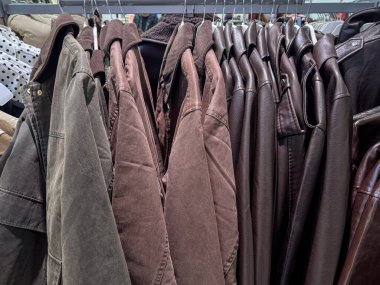 Çeşitli kahverengi ve toprak tonlu ceketlerle dolu bir elbise askısı sıkıca sergileniyor.