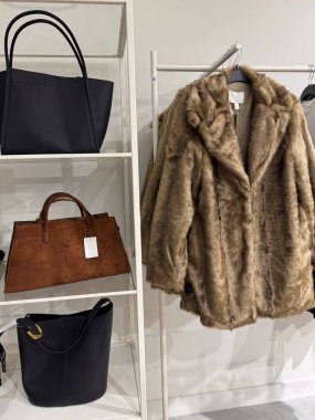 Zarif bir butik ortamında zarif el çantalarının raflarının yanında asılı yumuşak kahverengi bir kürk manto.