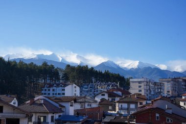 Çam ormanlarına ve açık mavi gökyüzünün altında karlı dağ zirvelerine karşı kümelenmiş çatıları olan küçük bir kasaba.