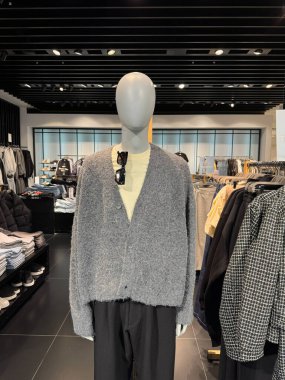 Tarafsız gri hırka giysisi çağdaş giyim mağazasındaki mankenlerde sergileniyor.