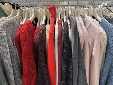 Rahat giyim mağazasının içinde askıda asılı renkli örülü kazaklar.