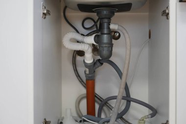 Mutfak dolabındaki boruların ve drenaj sisteminin altında.