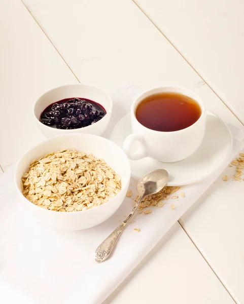 Beyaz arka planda frenk üzümü reçelli beyaz çay ve bir tabak yulaf ezmesi.