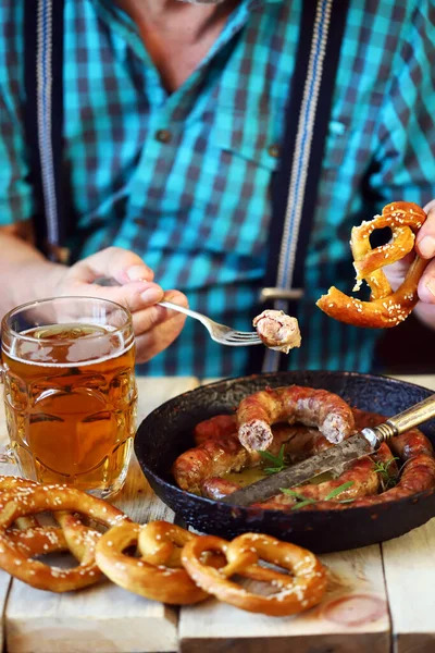 A man in a bar eats sausages and pretzels with beer. Oktoberfest menu.