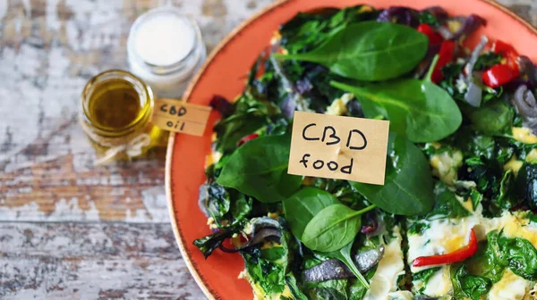 Note with the words cbd food in a pan with an omelet. Omelet with spinach and vegetables containing cannabis.