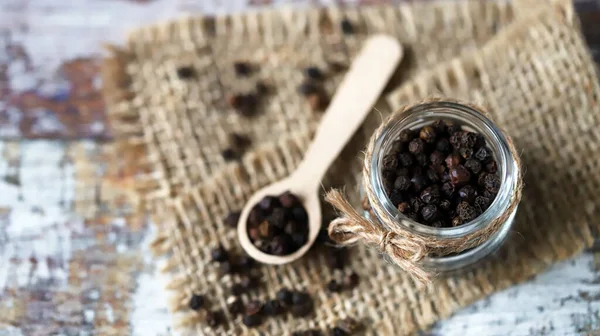 Black pepper peas. Black pepper in a jar and in a wooden spoon.