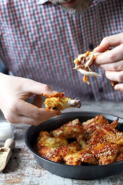 Bir adam elleriyle tavuk kanadı yer..