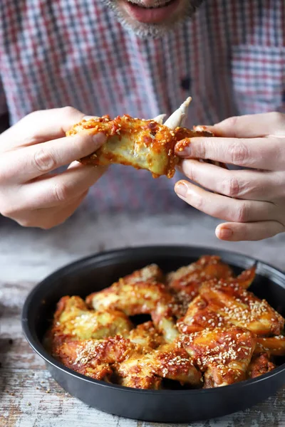 Bir adam elleriyle tavuk kanadı yer..