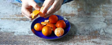Erkeklerin elleri mandalinayı soyuyor. Tabakta mandalina. Mandalina kabukları.