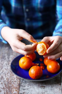 Erkeklerin elleri mandalinayı soyuyor. Tabakta mandalina. Mandalina kabukları.
