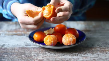 Erkeklerin elleri mandalinayı soyuyor. Tabakta mandalina. Mandalina kabukları.