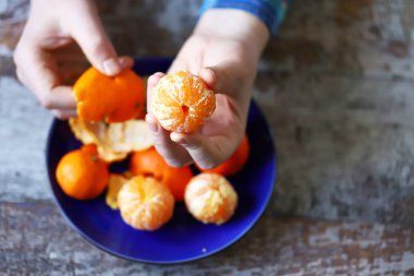 Erkeklerin elleri mandalinayı soyuyor. Tabakta mandalina. Mandalina kabukları.