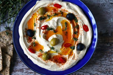 Zeytin, acı biber ve kekik ile mavi bir tabakta humus. Seçici odak.