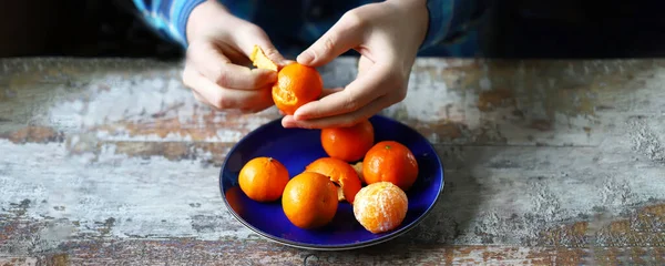 Peeling tangerines. Men\'s hands are peeling mandarin. Tangerines in a plate.